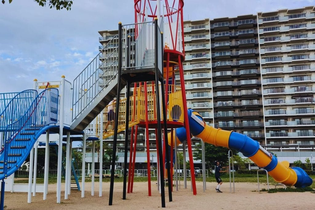 Large colourful slide and climbing frame at Port Island Kita Park playground in Kobe, Japan, with high-rise apartments in the background