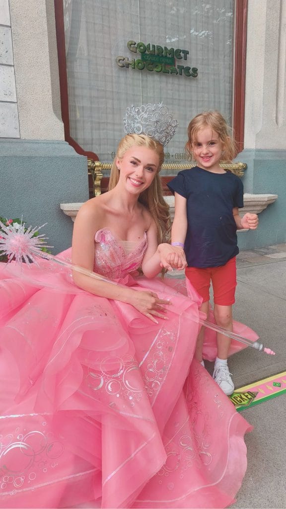 Child meeting Glinda the Good Witch from Wicked at Universal Studios Japan, smiling and holding hands outside a themed chocolate shop