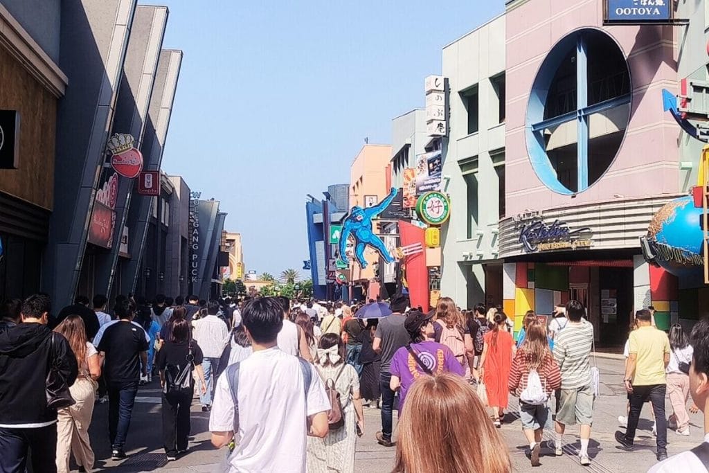 Crowds walking through Universal CityWalk Osaka on a sunny day, heading toward the entrance of Universal Studios Japan
