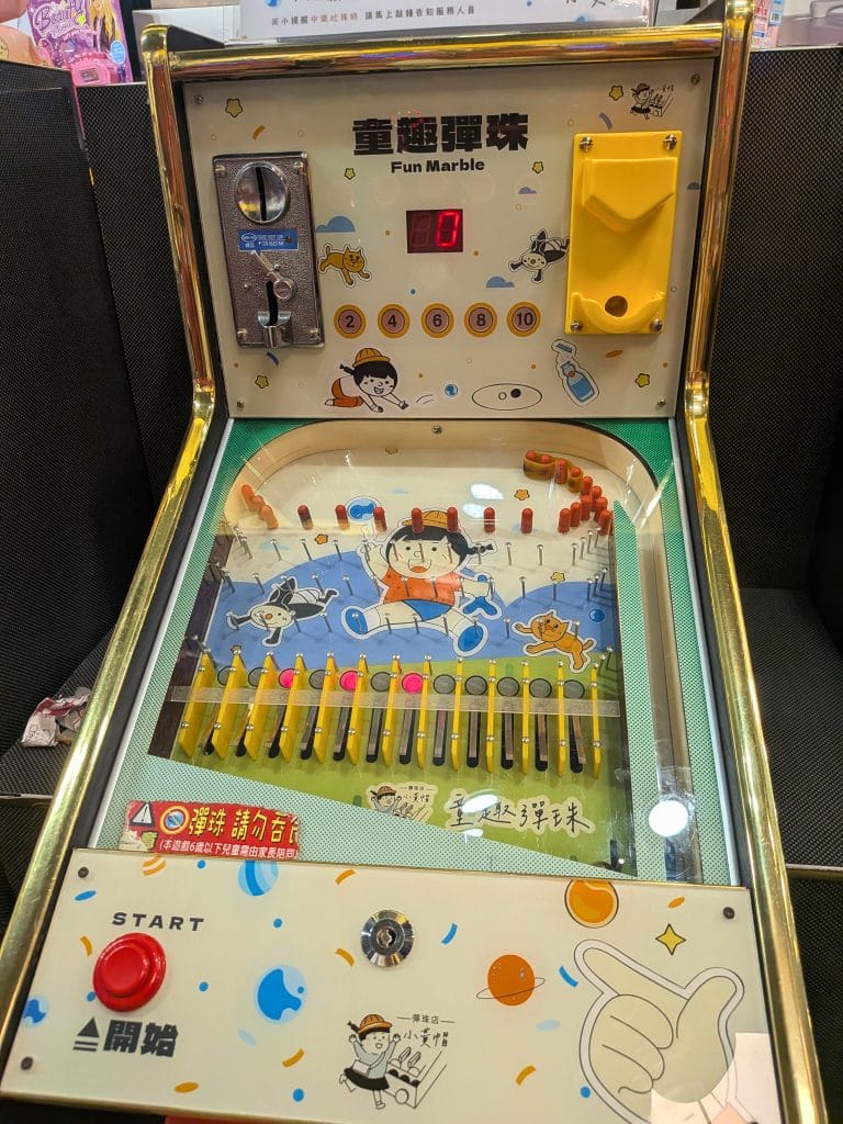 Taiwanese Blinker Ball arcade machine labeled "Fun Marble", featuring a colourful design with numbered slots (2, 4, 6, 8, 10), steel ball launcher, flashing lights, and cartoon graphics aimed at children. A popular family arcade game known locally as 小鋼珠機 (xiǎo gāng zhū jī).