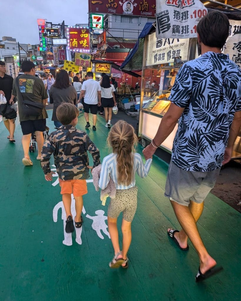 Family walking through Kenting Night Market in Taiwan, surrounded by food stalls, neon signs, and a lively evening crowd