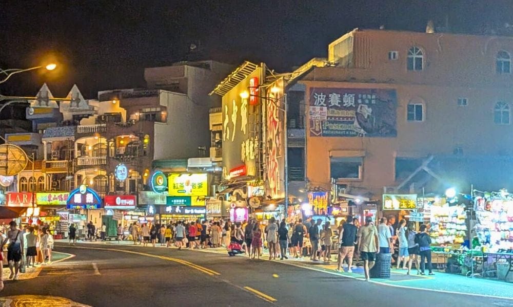 Busy evening scene at Kenting Night Market with colourful lights, food stalls, and crowds lining the street.