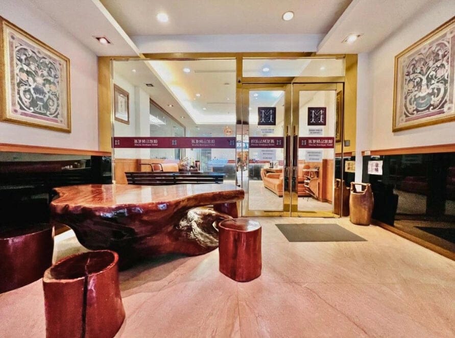 Reception area of Mucha Boutique Hotel in Yilan, featuring a polished wood table with matching stools, glass entrance doors, and warm lighting.