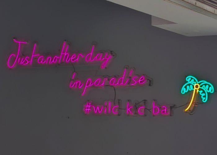 Neon sign reading “Just another day in paradise” at Cowboy’s Bar on South Beach, Kenting – popular family-friendly spot with Wi-Fi and BBQ.