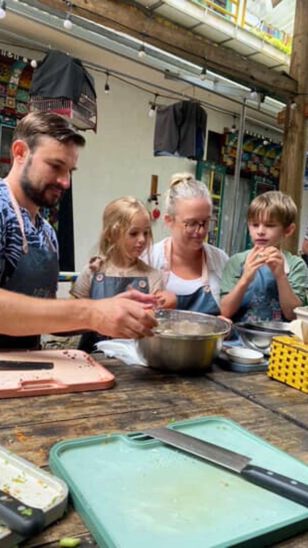 Family cooking class in Vietnam – parents and young children learning to prepare traditional dishes together at an outdoor kitchen table