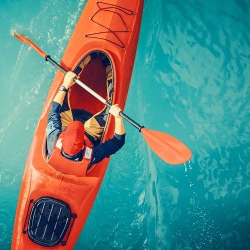 Aerial view of a person paddling a bright red kayak across clear turquoise water in Okinawa