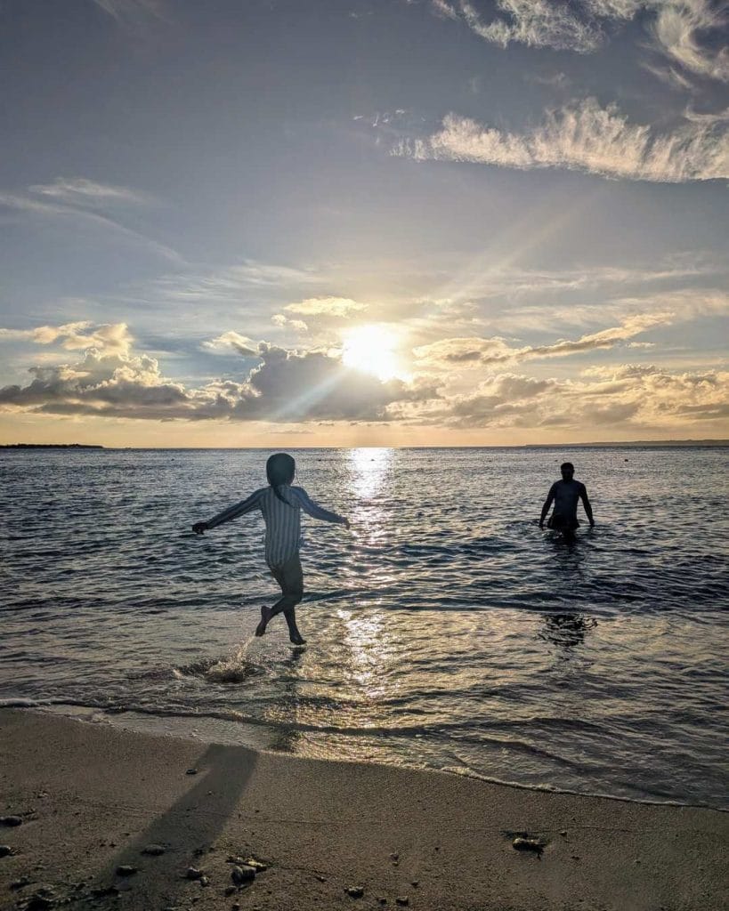 Silhouette of a child playing in the water at sunset on Sesoko Beach, Okinawa, with golden light reflecting across the sea.