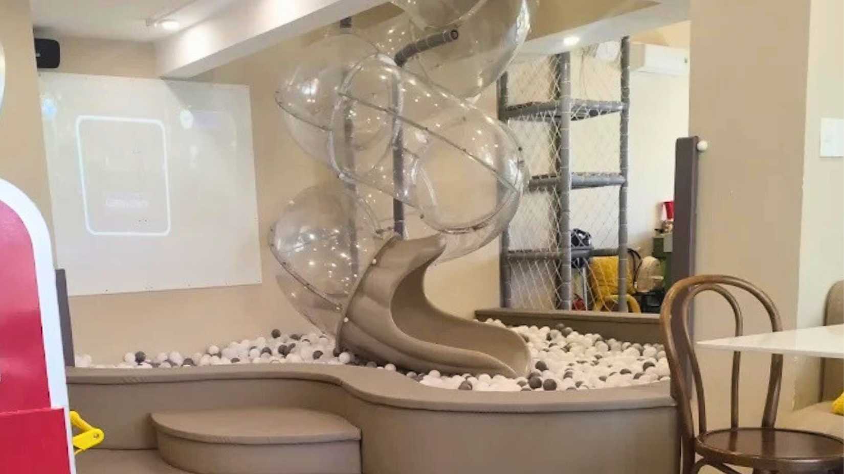 Indoor kids’ play area at Namto Premium Kids Café in Da Nang, featuring a clear tube slide leading into a ball pit next to café seating.
