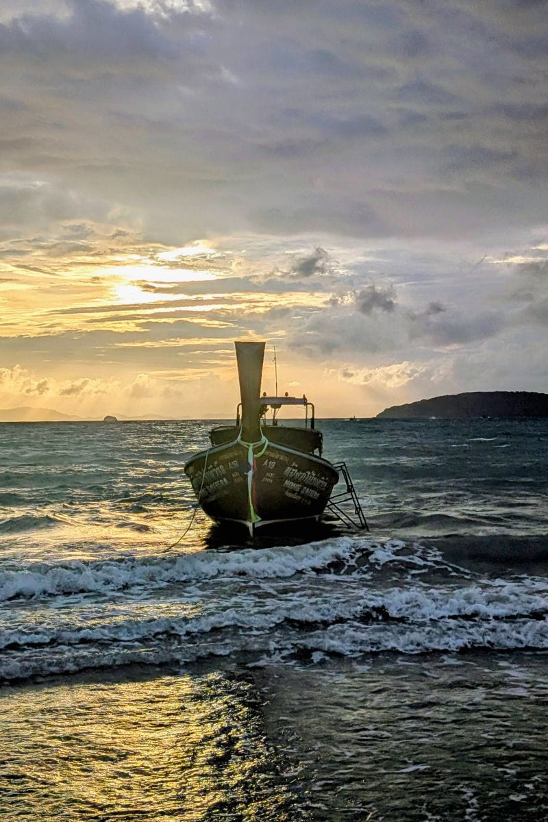 Longtail boat arriving at Railay Beach Thailand with limestone cliffs behind